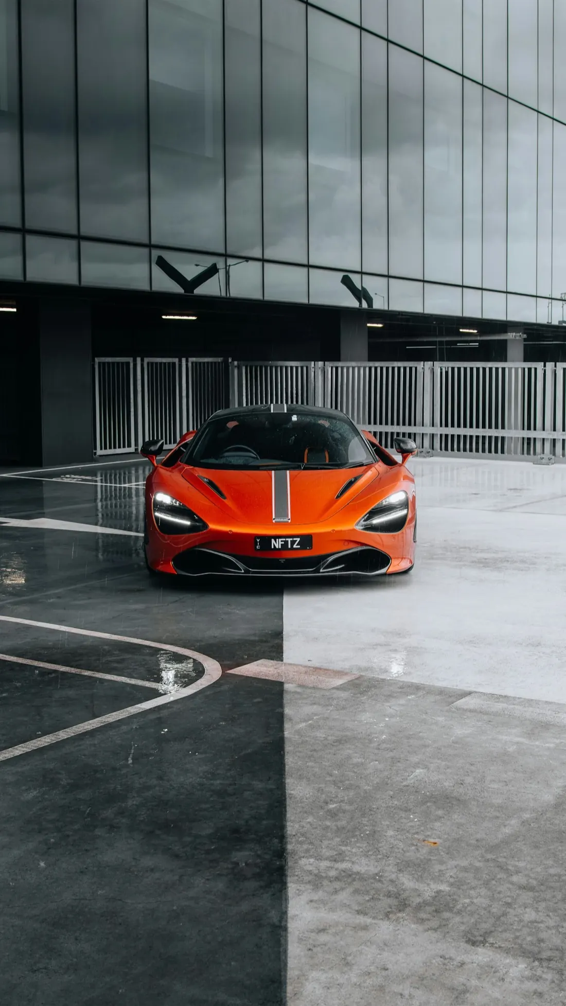 An orange McLaren 720S parked in front of a dark glass building