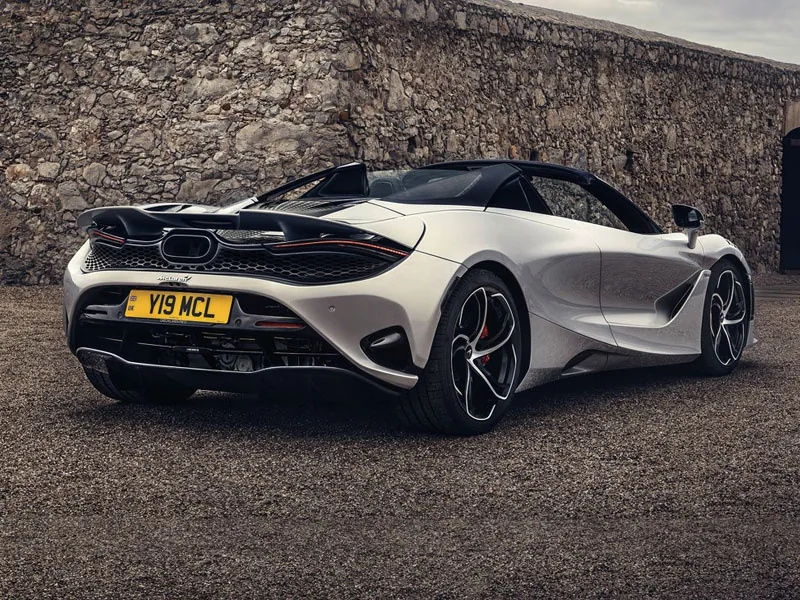 A white McLaren with its rear wing raised on a coast road